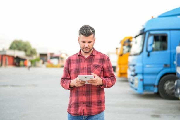 A fleet owner is in the lot of his business with trucks parked behind him as he reviews the analytics from his fuel card from the dashboard on his tablet.