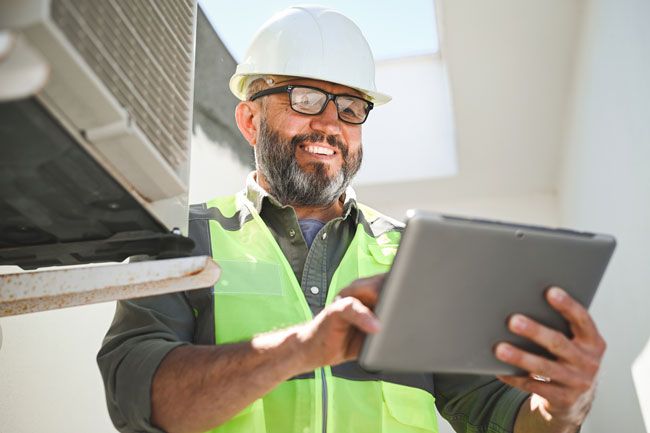 An HVAC owner wears a hard hat and reviews the fleet fuel card data from his tablet.