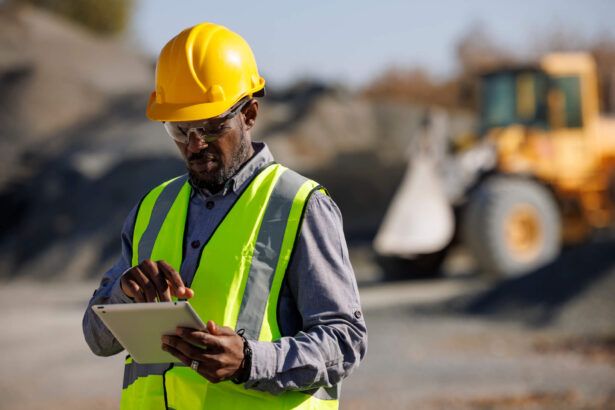 A construction company owner wears a hard hat on a construction site and reviews fuel card transactions on his tablet.