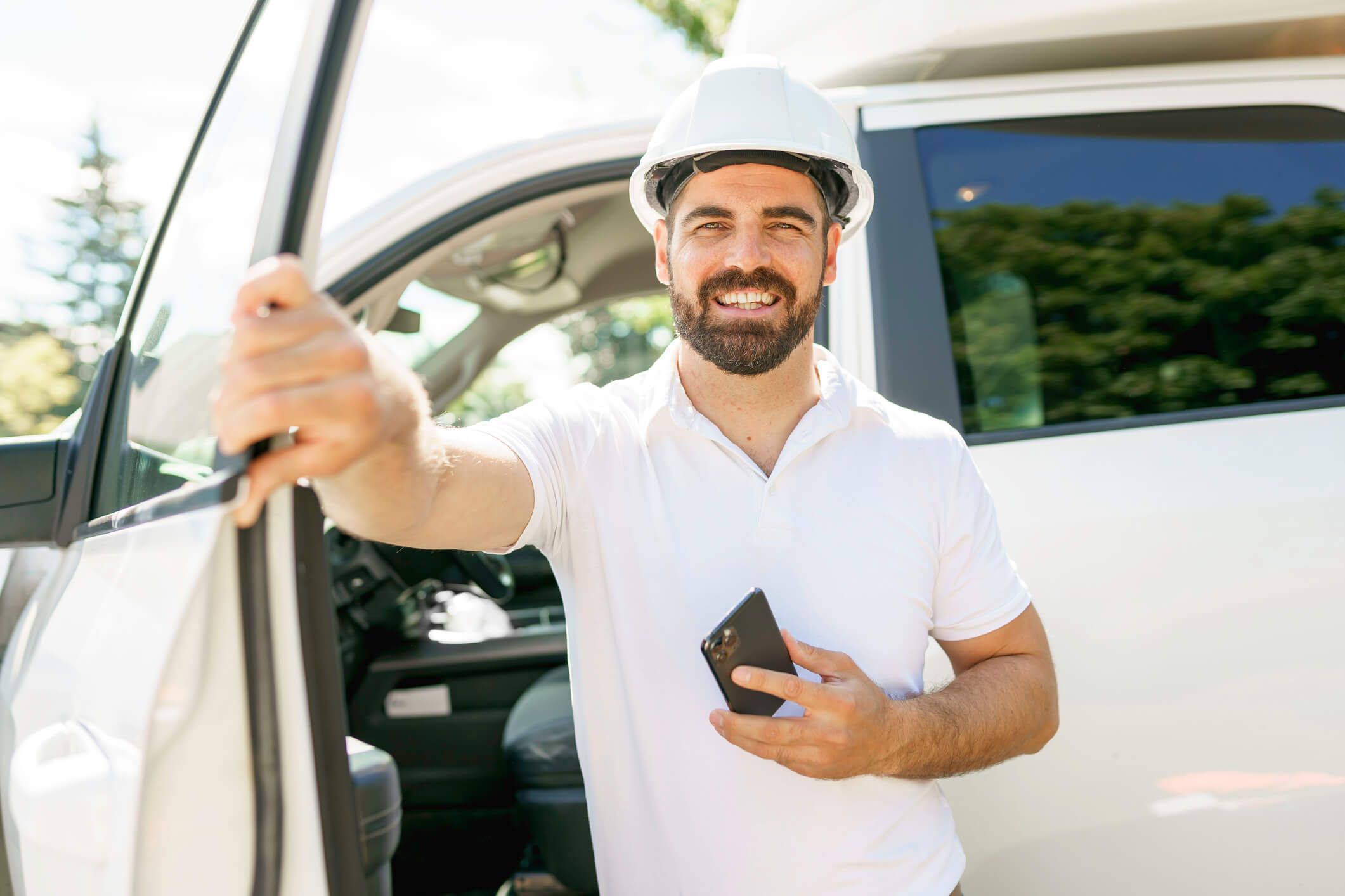 A construction worker exits his vehicle with his phone.