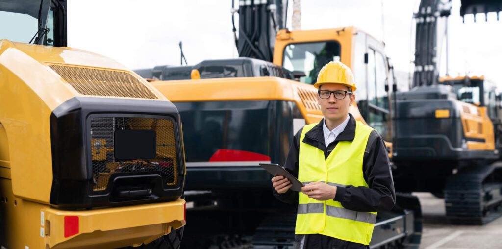 A contractor reviews analytics of his fleet’s fuel card usage while wearing a hard hat in front of construction vehicles.