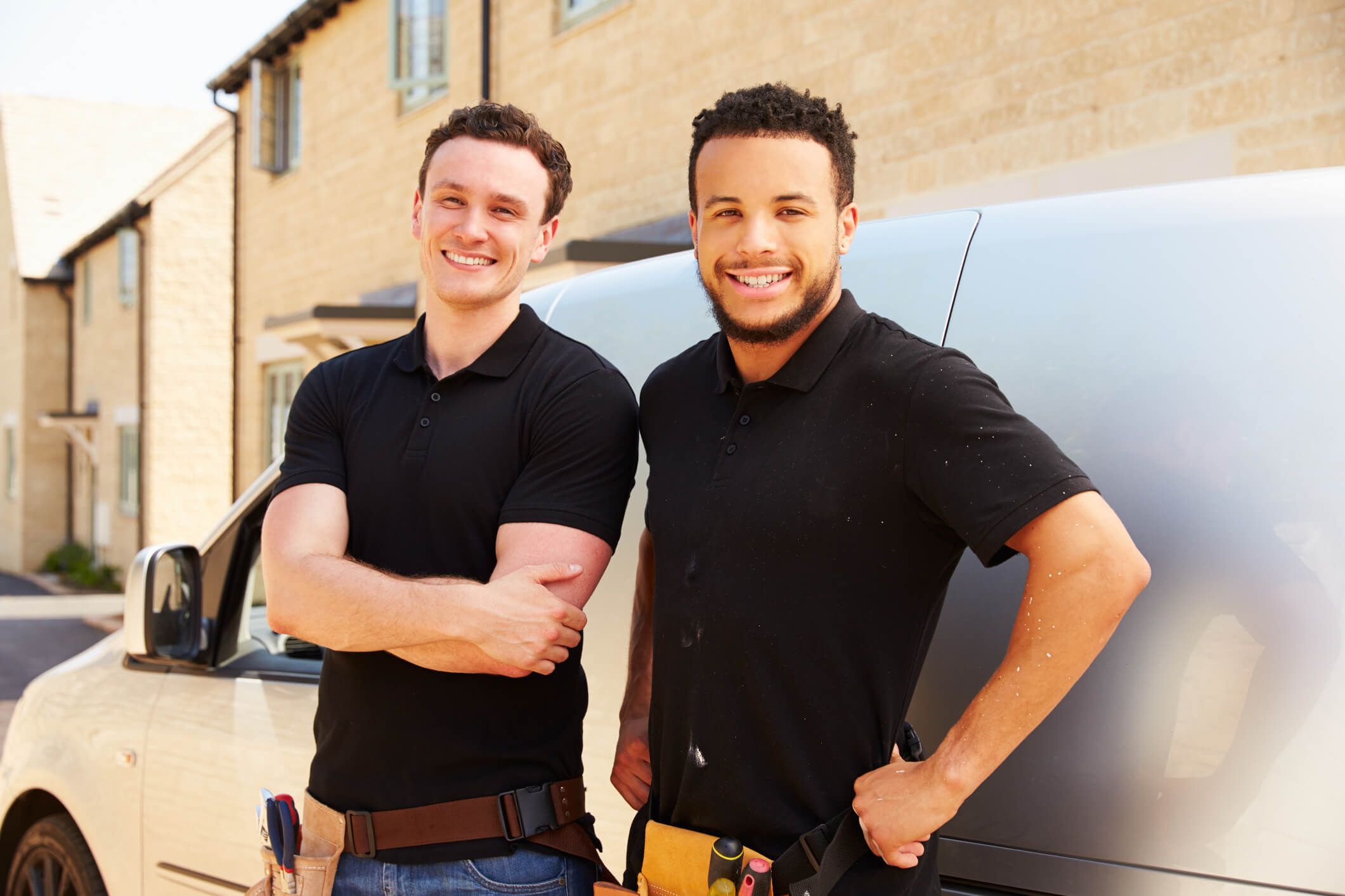 Two plumbers stand side-by-side next to the van from their business fleet.