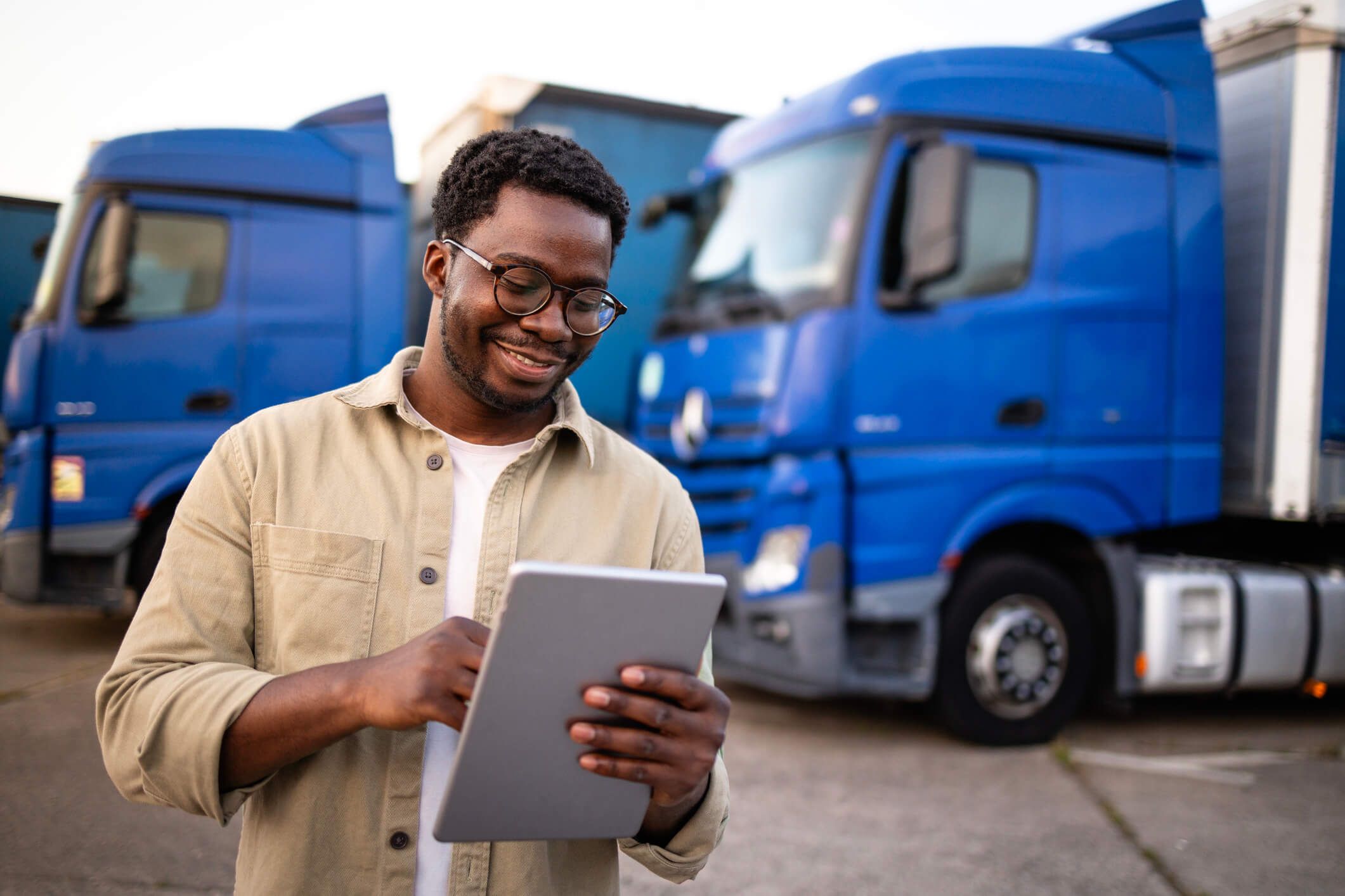 A wholesaler stands outside reviewing the analytics from his fleet card while in front of his fleet of trucks.
